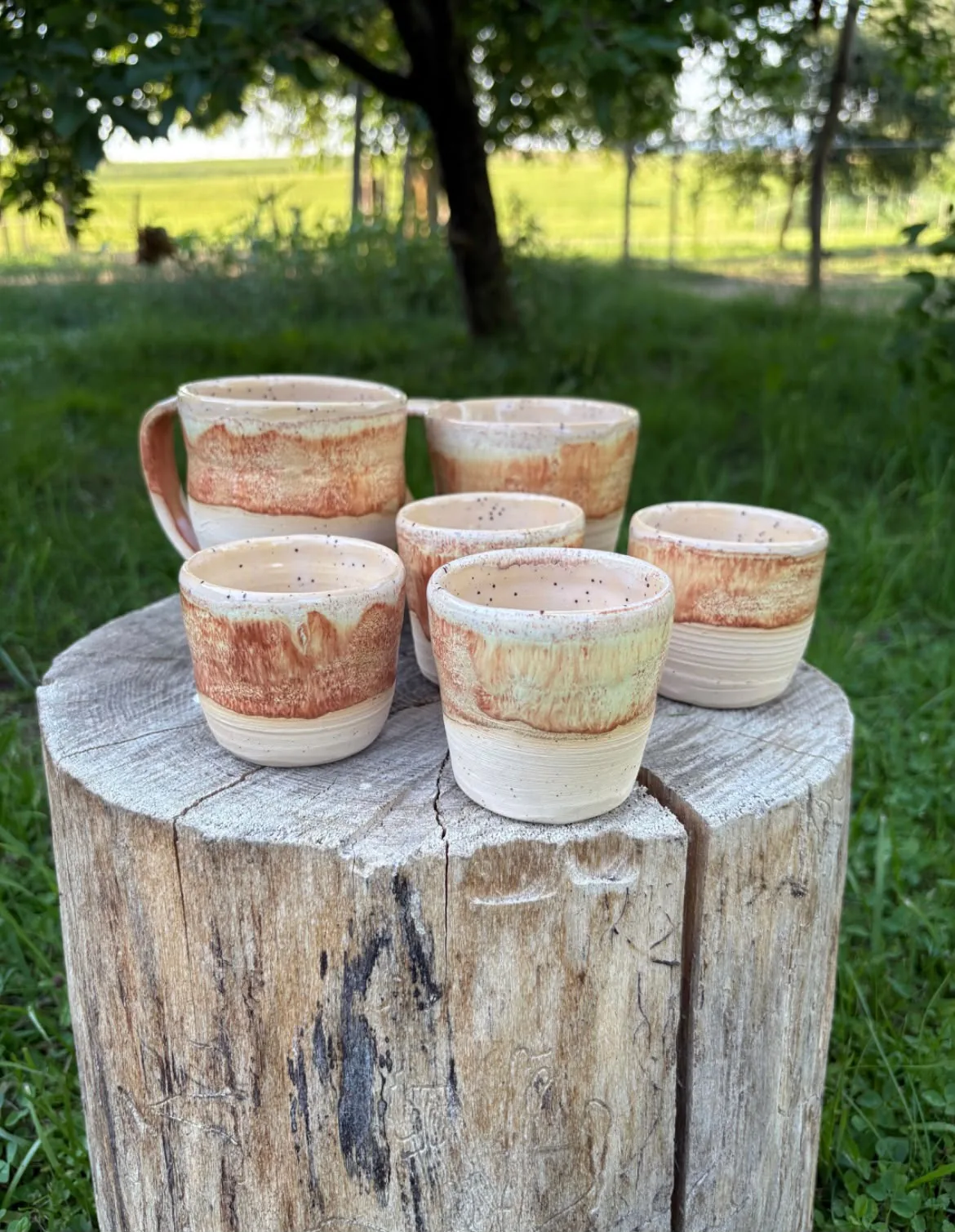 Handgetöpfertes Keramikbecher-Set in erdigen Tönen auf einem Holzstamm