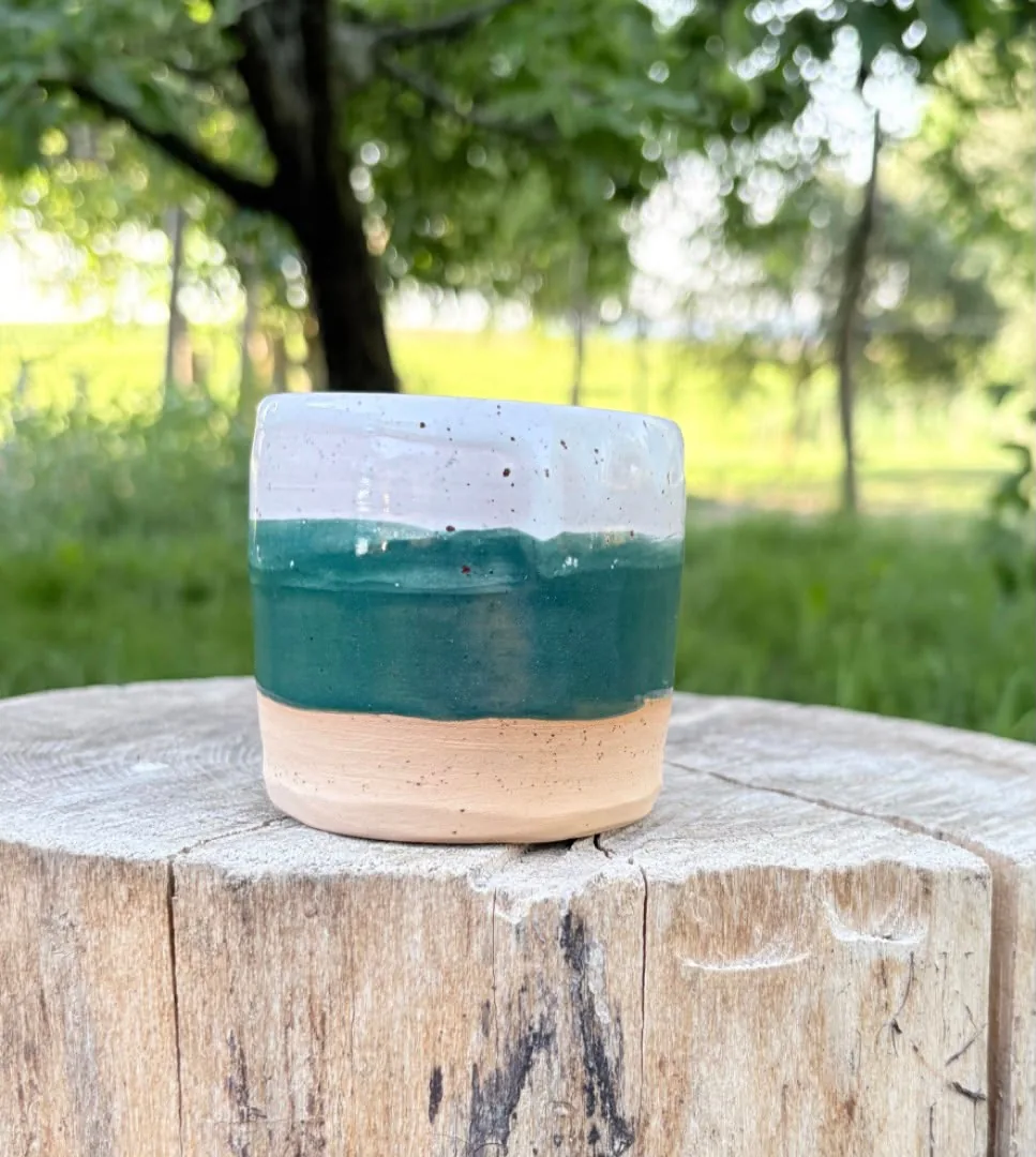 Handgetöpferter Becher mit waldgrüner und weißer Glasur auf einem Holzblock