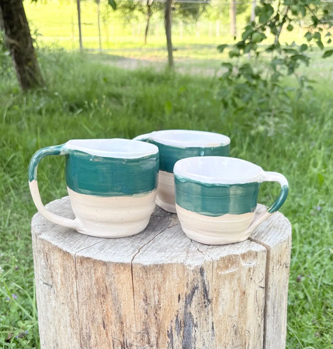 Drei handgetöpferte Tassen mit waldgrüner Glasur auf einem Holzstamm