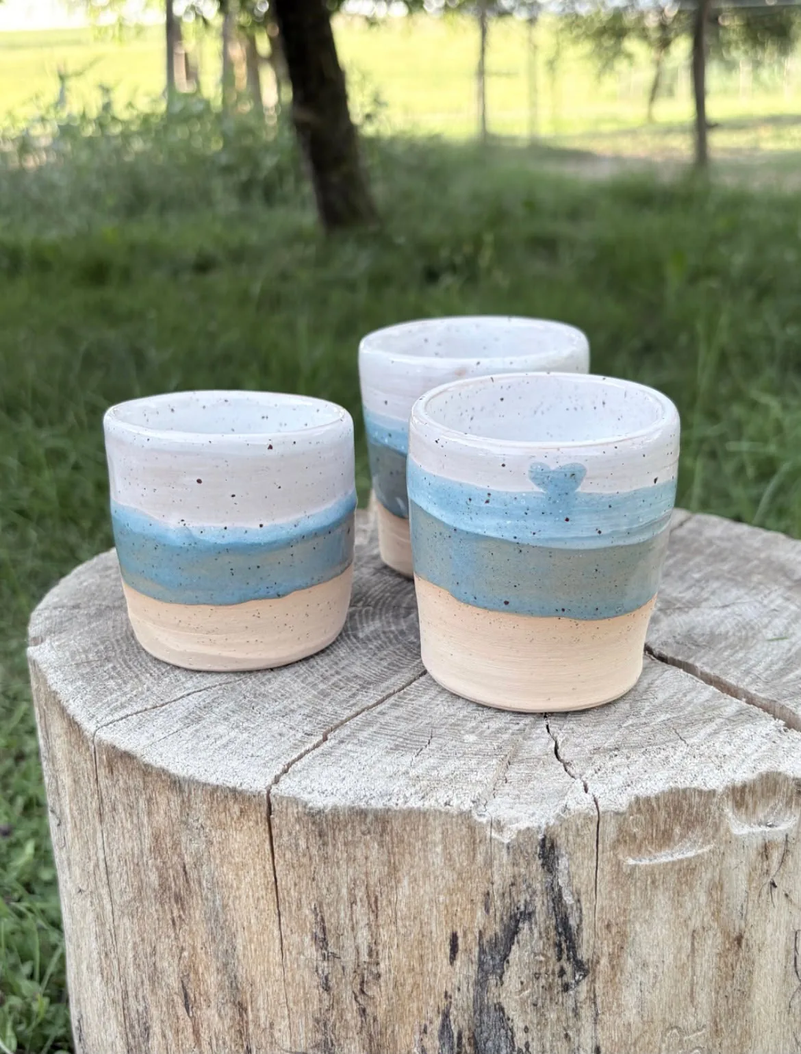 Drei handgetöpferte Becher in Weiß und Hellblau mit kleinem Herzdekor auf Holz